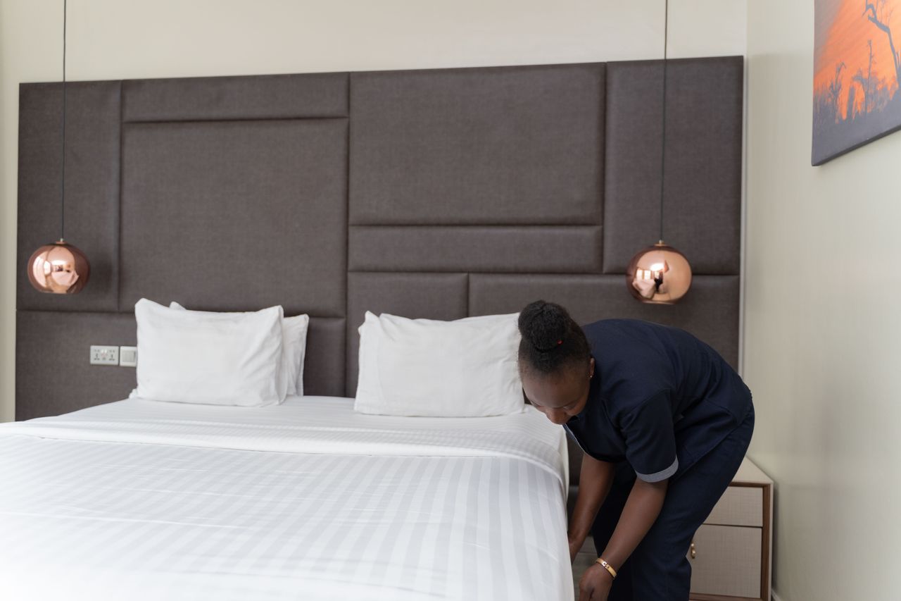 The Art of Drawing Readers In: Your attractive post title goes here A hotel staff member prepares a bed in a sleek, modern hotel room with copper accents.